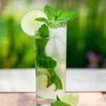 Tall clear highball glass full of the best mojito recipe, garnished with mint and a slice of lime.