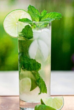 Tall clear highball glass full of the best mojito recipe, garnished with mint and a slice of lime.