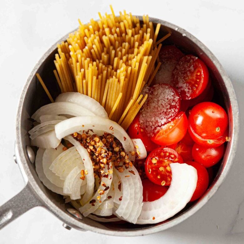 Adding all the ingredients for One Pot Pasta into the same silver pot to cook on the stove.