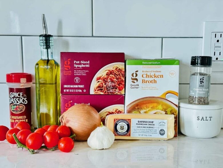 Ingredients for one pot pasta including dry linguine, cherry tomatoes, garlic, basil, and rotisserie chicken on a kitchen counter.