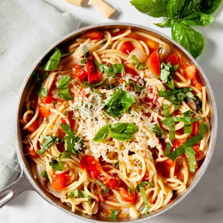 Close up of One Pot Tomato Basil Pasta in a serving bowl, topped with spinach leaves.