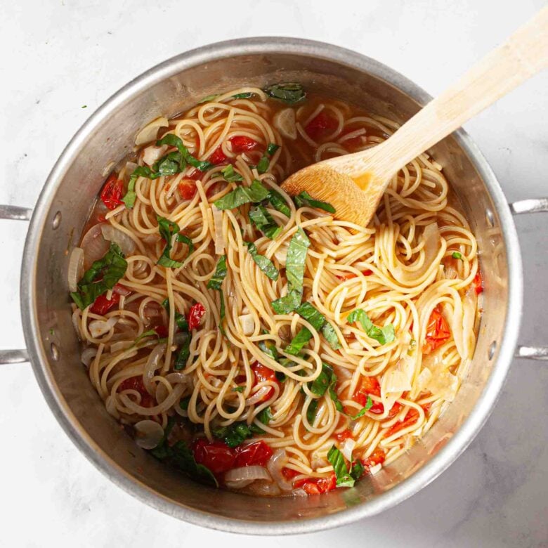 Wooden spoon in silver pot, stirring the pasta noodles and other ingredients.