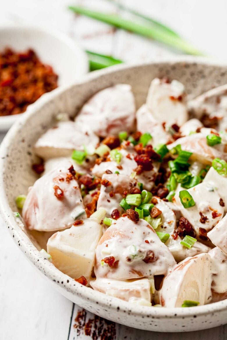 Round white bowl full of Ranch Potato Salad, topped with bacon and chives.