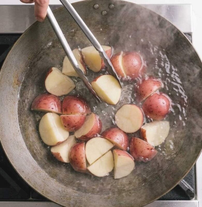Boiling the potatoes in a pan so that they're tender and ready to add to the salad.