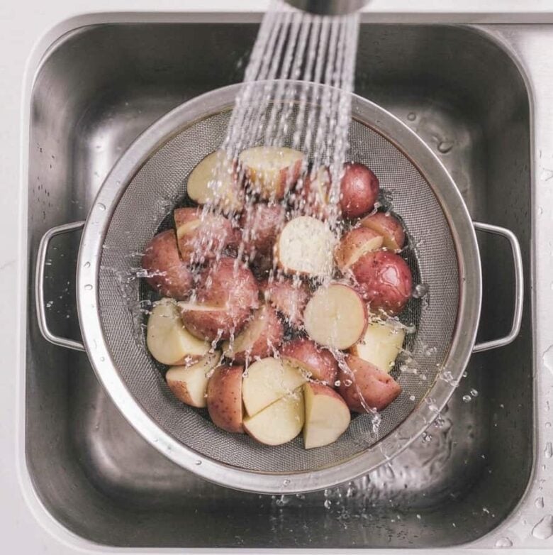 Washing off the sliced potatoes in a colander using the sink faucet.