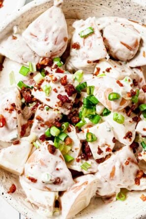 Close up of Bacon Ranch Potato Salad topped with bacon and green onions in a white round bowl.