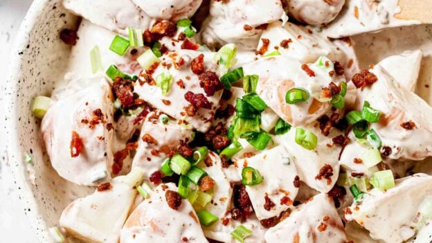 Close up of Bacon Ranch Potato Salad topped with bacon and green onions in a white round bowl.