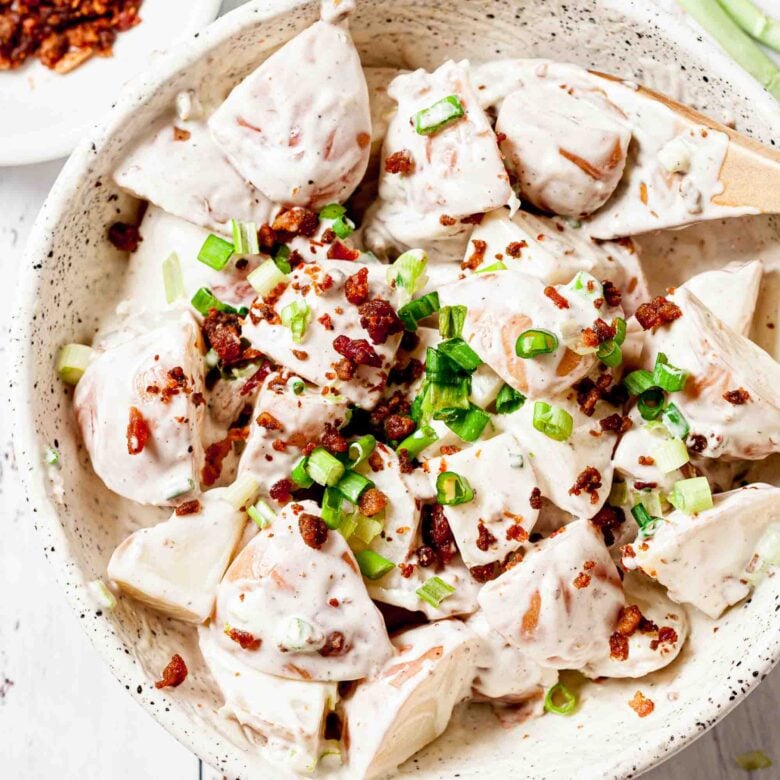 Close up of Bacon Ranch Potato Salad topped with bacon and green onions in a white round bowl.
