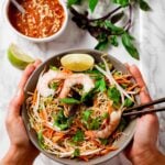 Hands holding a serving bowl full of thin rice noodles and jump shrimp to create a spring roll bowl.