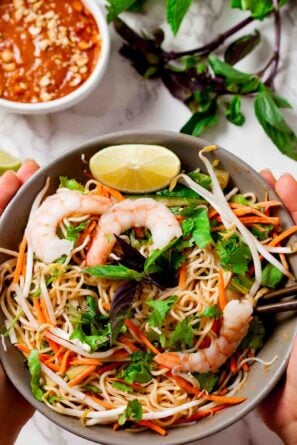 Hands holding a serving bowl full of thin rice noodles and jump shrimp to create a spring roll bowl.
