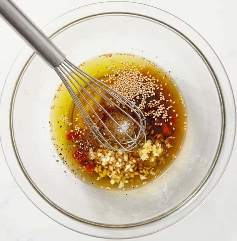 Mixing the dressing ingredients for the Asian Pasta Salad in a clear glass bowl using a whisk.