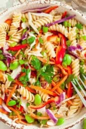 White bowl full of cooked asian pasta salad with a silver fork getting ready to take a scoop.