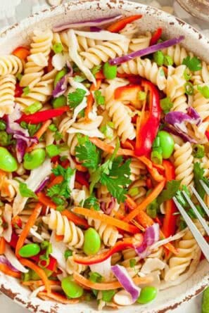 White bowl full of cooked asian pasta salad with a silver fork getting ready to take a scoop.
