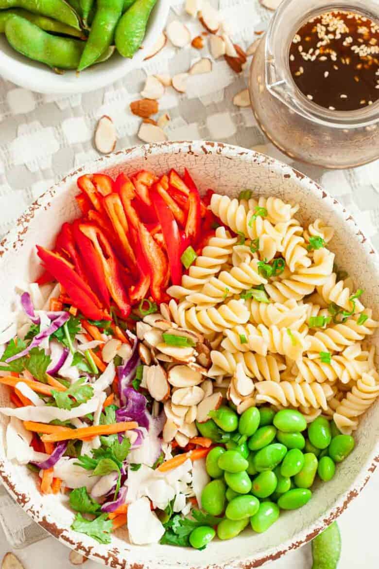 All the ingredients needed to make the pasta salad in a white bowl, getting ready to have the dressing added to the top.