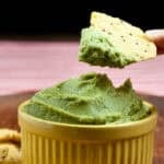 Hand holding tortilla chip and dipping it into a yellow bowl full of avocado hummus.