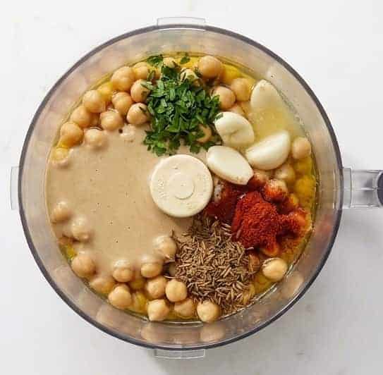 Adding all the ingredients to make avocado hummus into the food processor.