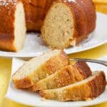 Banana pudding cake with bundt cake in background and 3 slices of cake on a white plate.