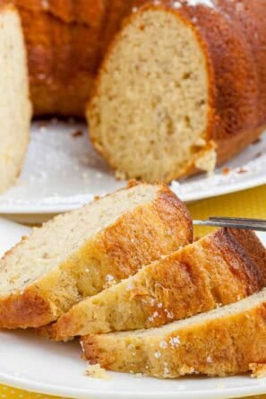 Banana pudding cake with bundt cake in background and 3 slices of cake on a white plate.