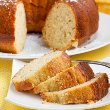 Banana pudding cake with bundt cake in background and 3 slices of cake on a white plate.