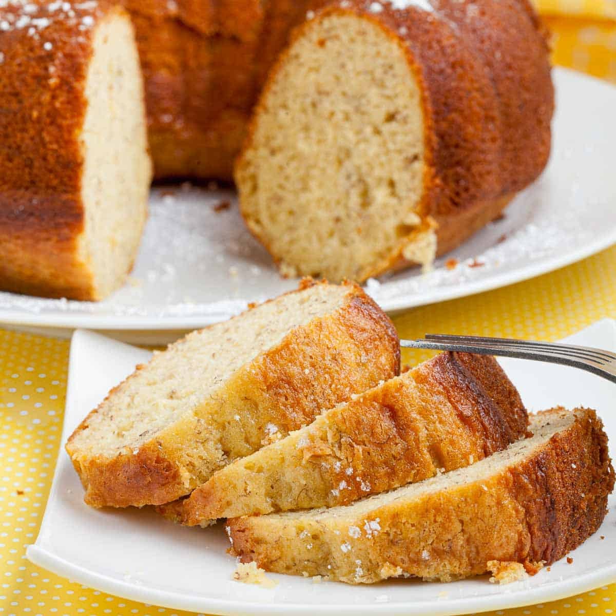 Banana pudding cake with bundt cake in background and 3 slices of cake on a white plate.