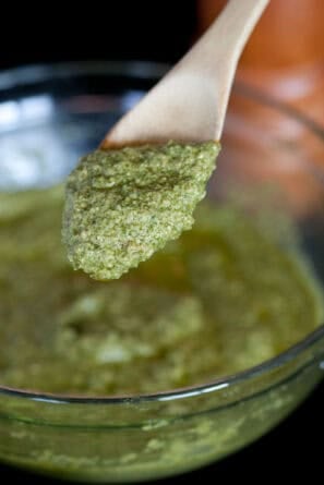 Brown spoon in a clear bowl scooping out pesto.