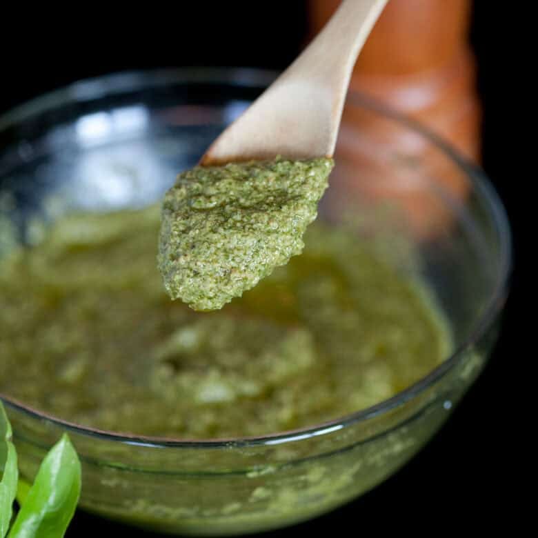 Brown spoon in a clear bowl scooping out pesto.