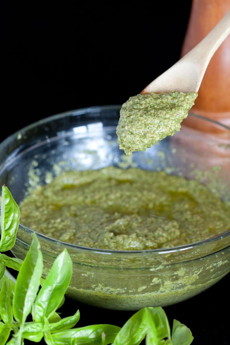 Brown spoon dipping in a clear bowl to pull out a spoonful of Basil Pesto Recipe.