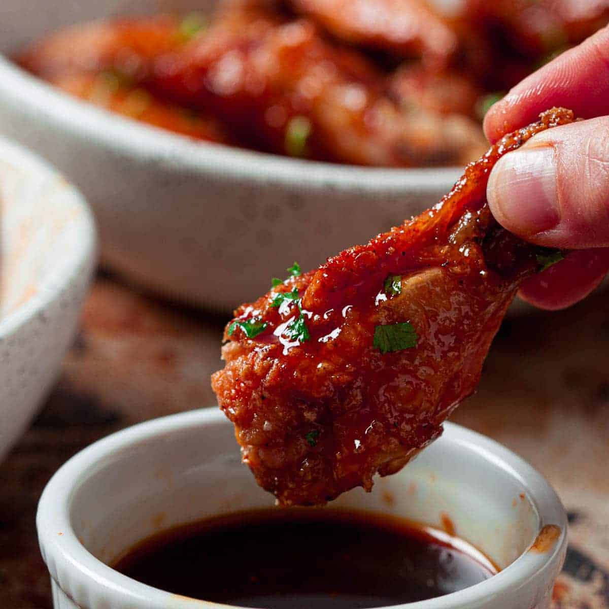 Hand holding a buffalo chicken wing and dipping it into a small white bowl of the extra dipping sauce.