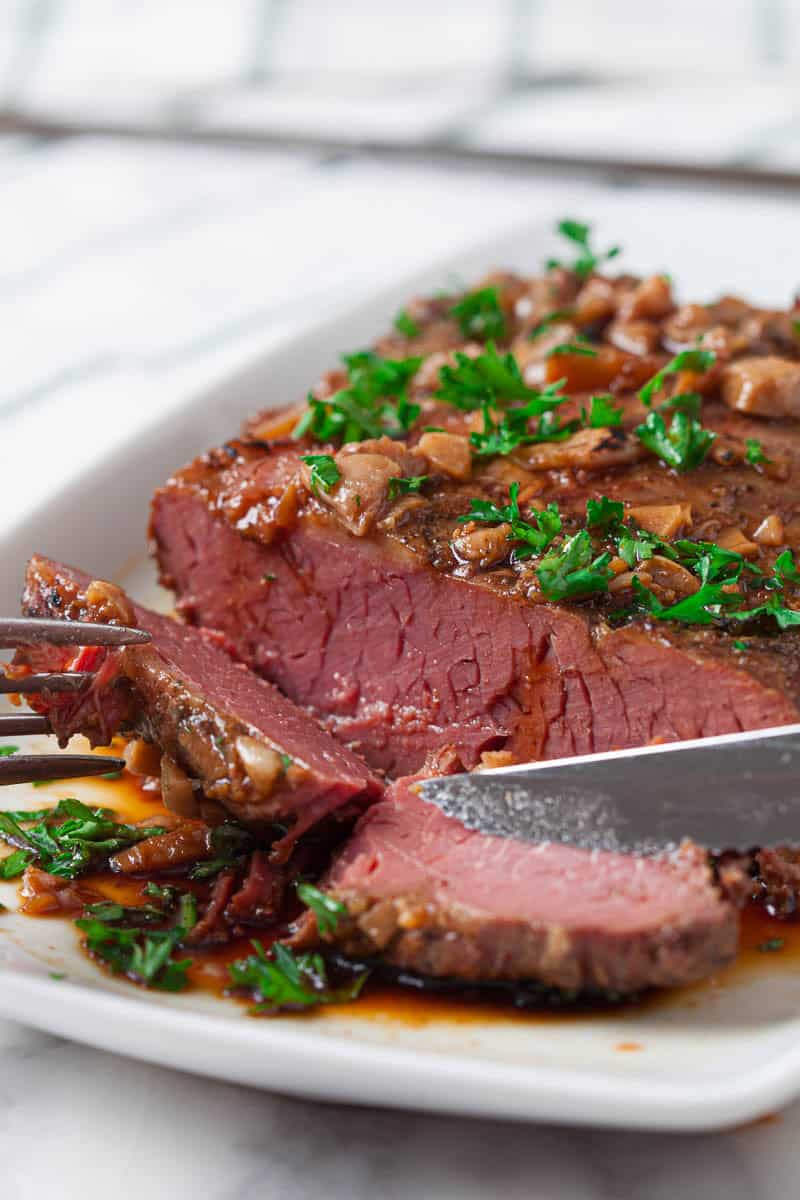 Slow Cooker Brisket on a white platter being sliced into with a sharp carving knife.