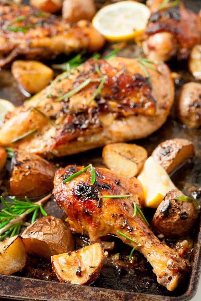 Close up of greek chicken on a pan, surrounded by potatoes.