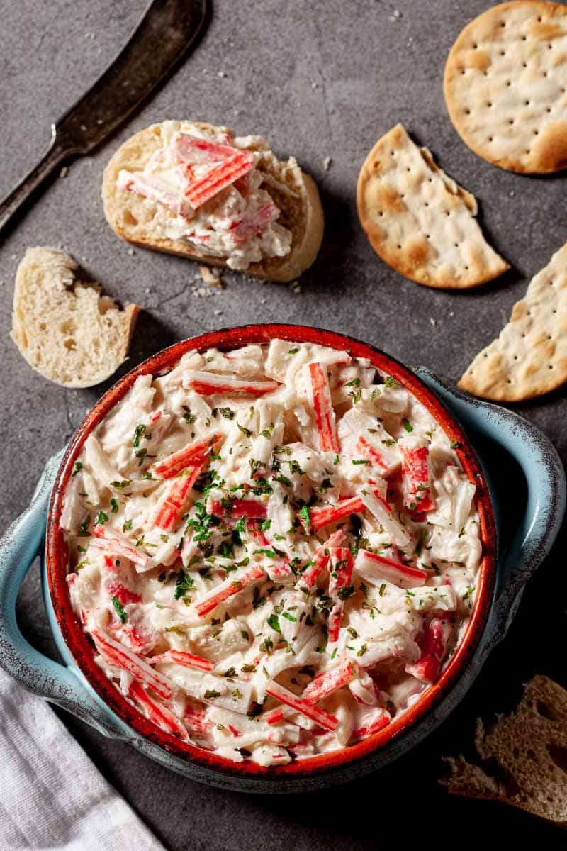 Bowl of imitation crab dip with pieces of bread next to the bowl.