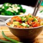 Brown bowl full of salmon poke bowl with brown chopsticks sticking out.