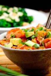 Brown bowl full of salmon poke bowl with brown chopsticks sticking out.