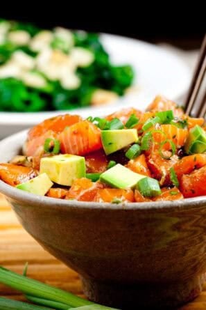 Brown bowl full of salmon poke bowl with brown chopsticks sticking out.