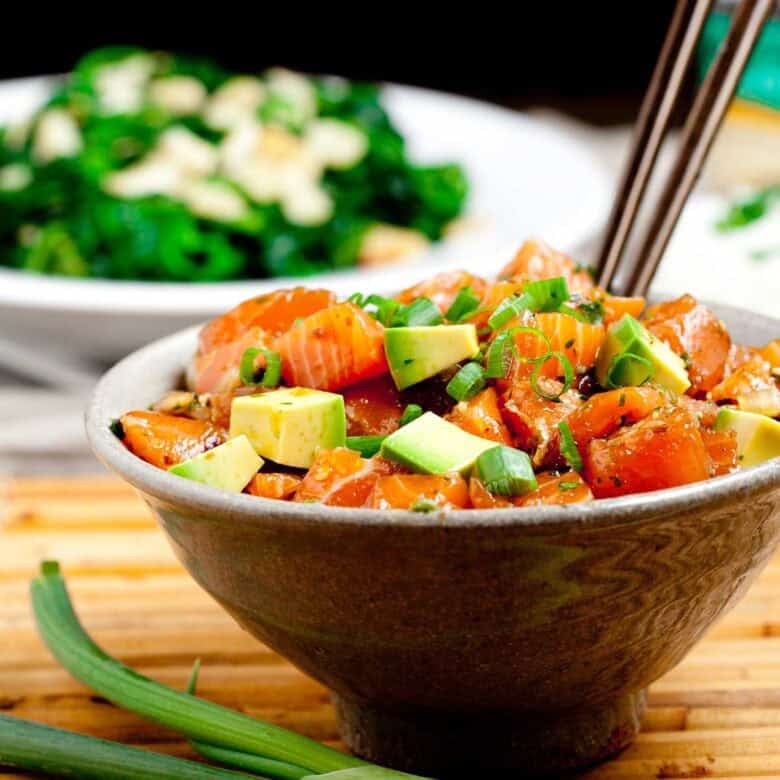 Brown bowl full of salmon poke bowl with brown chopsticks sticking out.