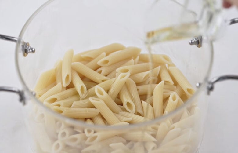 Drained pasta being drizzled with olive oil.