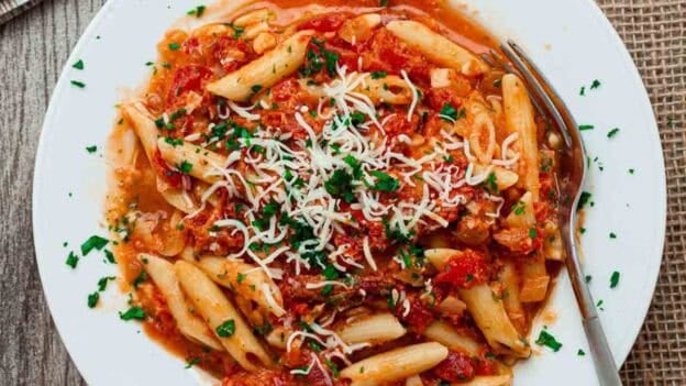 Overhead view of a white bowl full of sun dried tomato pasta.
