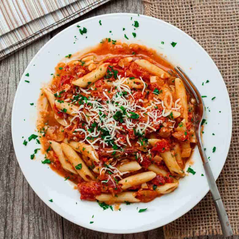 Overhead view of a white bowl full of sun dried tomato pasta.