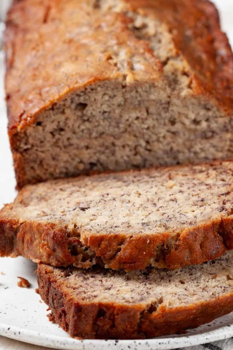 Banana bread loaf close up with two slices on a white plate.
