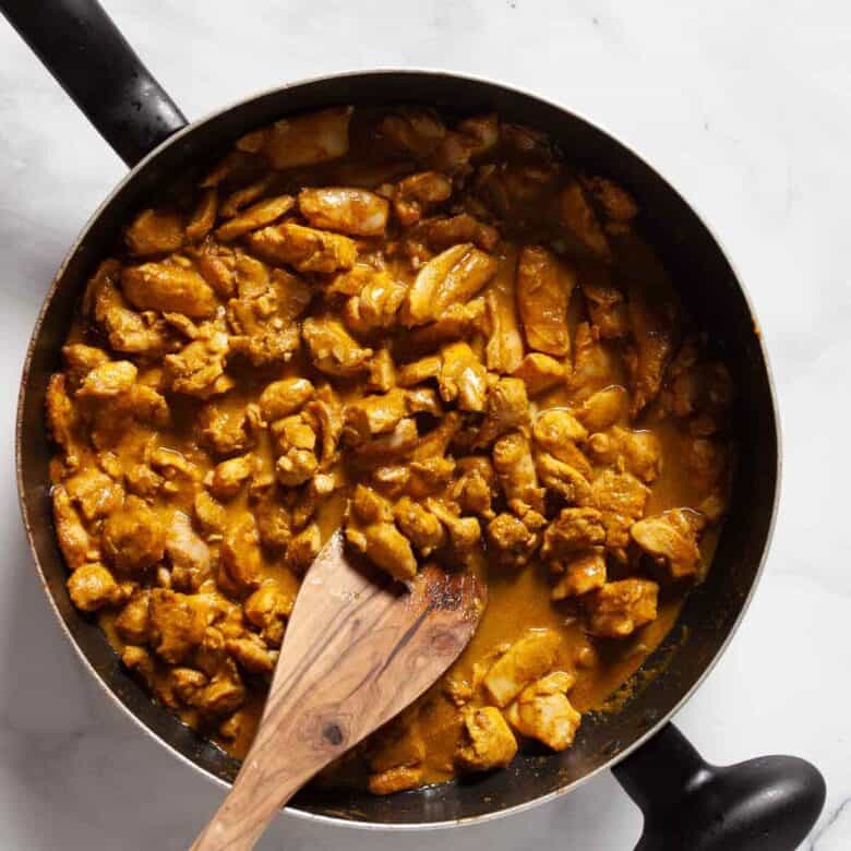 Sauce pan full of butter chicken, being stirred by a wooden spoon.