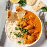 Butter Chicken in a white bowl with rice and pita bread.