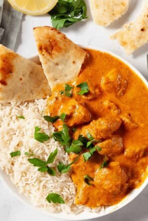 Butter Chicken in a white bowl with rice and pita bread.