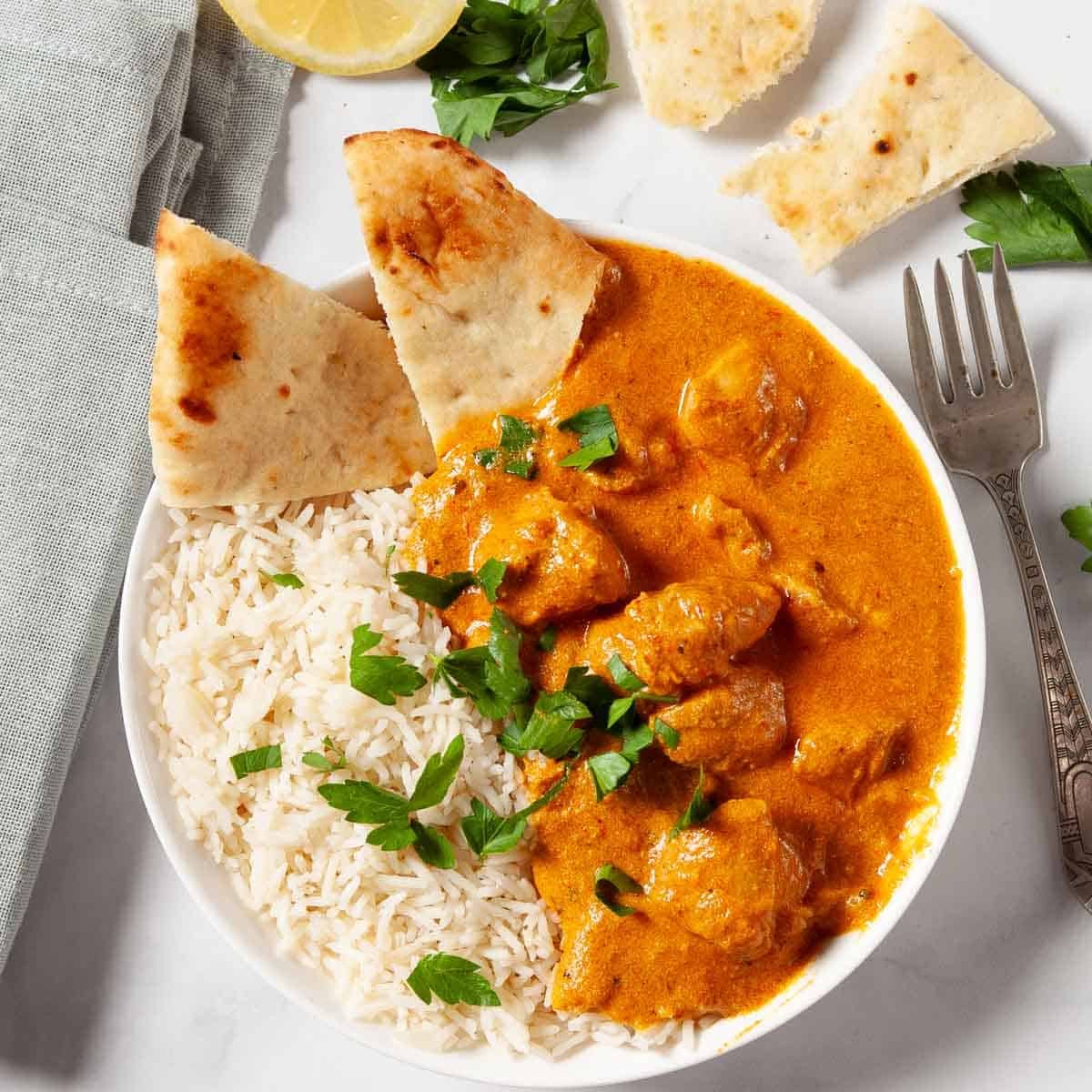 Butter Chicken in a white bowl with rice and pita bread.