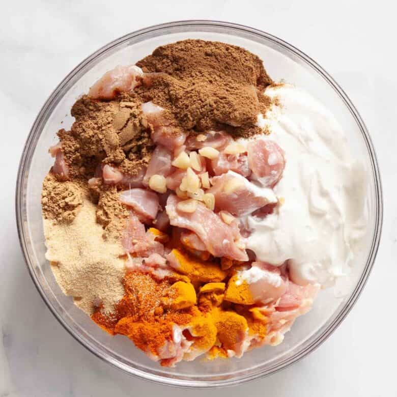 Adding the cut up chicken and ingredients into a clear glass bowl.