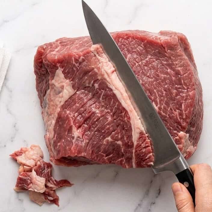 Using a sharp knife to trim off the excess fat of the brisket.