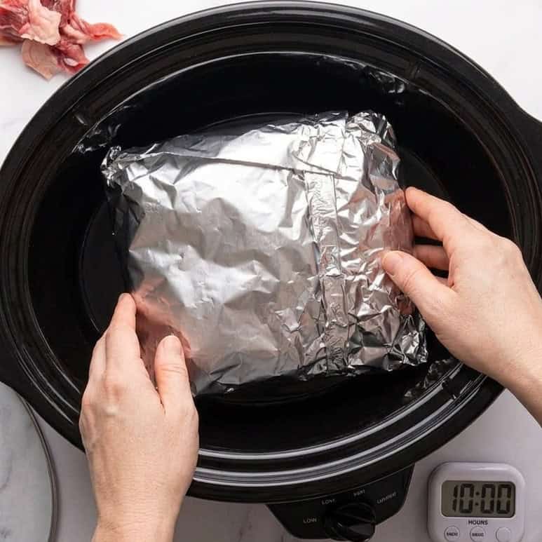 Placing the foil wrapped brisket in a slow cooker.