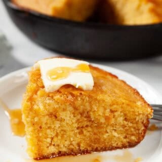 Close up of Honey Cornbread on a white plate topped with a cube of butter and a drizzle of honey.