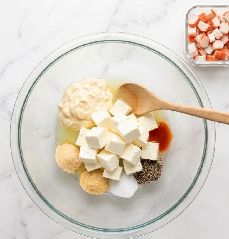 Adding the crab dip ingredients into a glass bowl and using a wooden spoon to stir.
