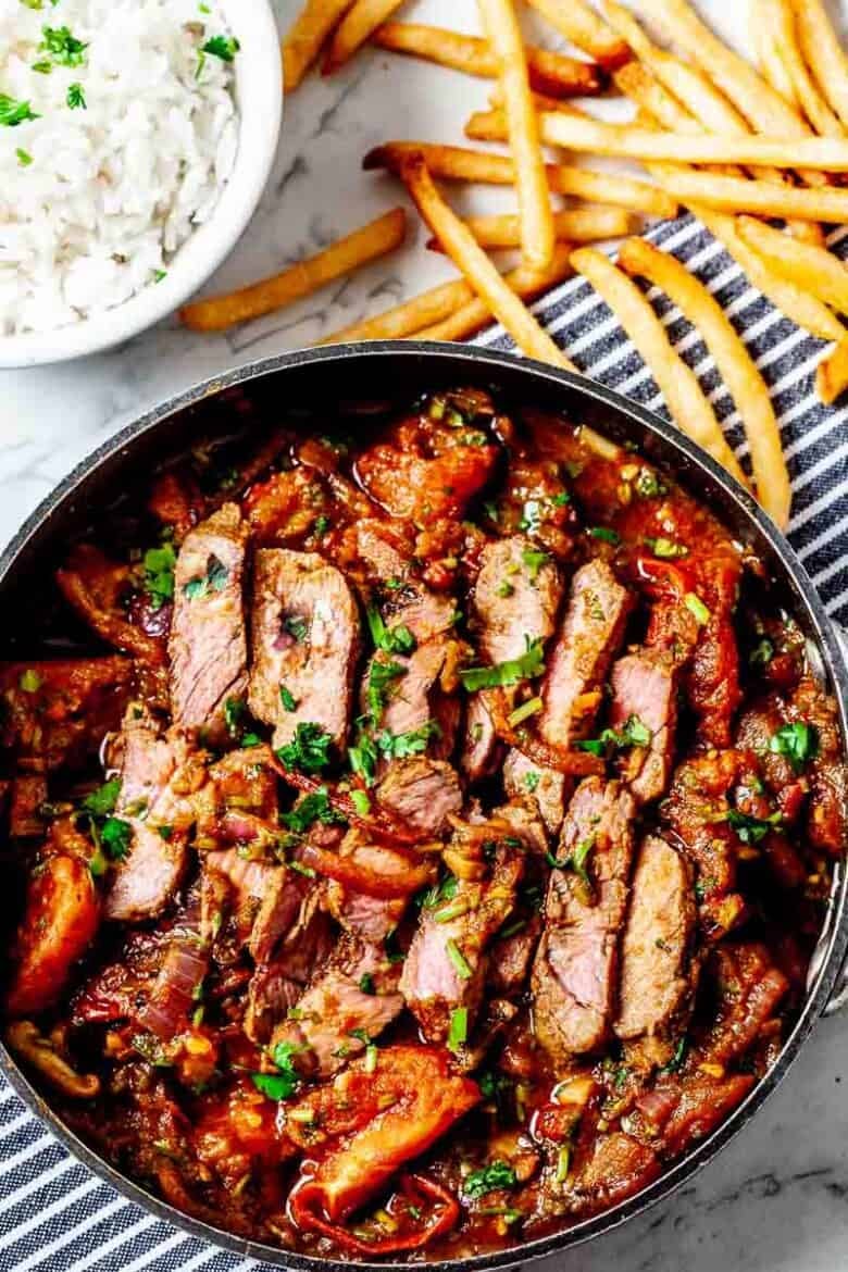 Overhead view of Lomo Saltado Recipe in a black serving bowl, paired with a side of fries and dip.