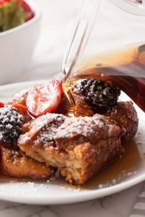 Overnight French Toast Casserole on a white plate with syrup being poured on top.